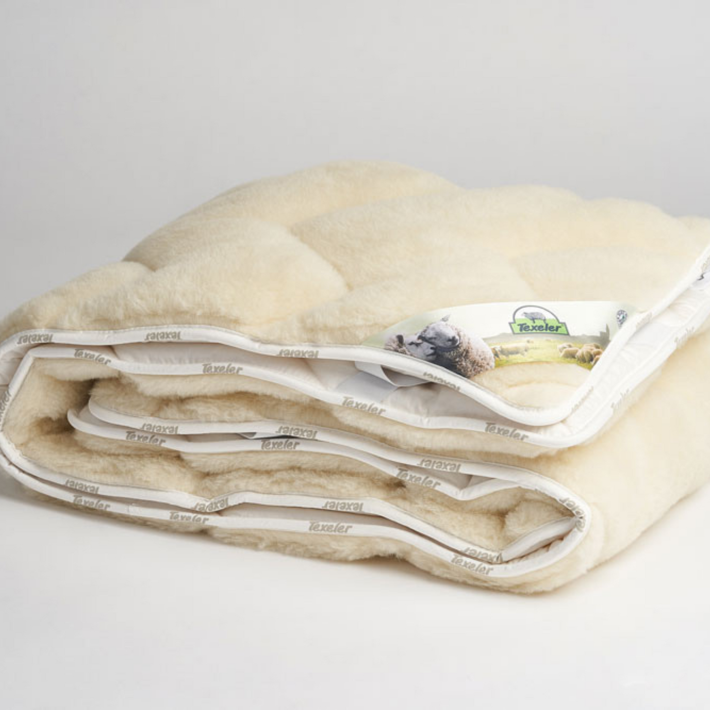 A folded beige mattress topper with a wool and cashmere layer on top. With a white/grey background. Brand name Texeler